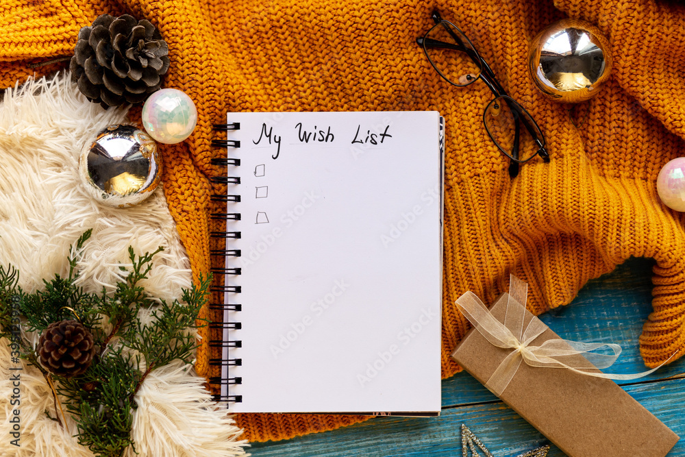 Fototapeta premium Flat lay New Year decorations ans blank white spiral notebook with My wish list framed with yellow cozy winter decor, tree branches, xmas toys. Planning,wish list 2021 concept