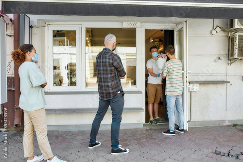 Full length shot of people wearing mask waiting, standing in line, respecting social distancing to collect their orders from the flower shop during coronavirus lockdown