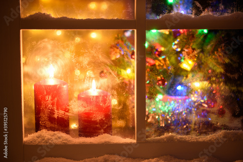 Night view from outside of a window decorated for Christmas. Lit candles, defocused Christmas tree and lights.