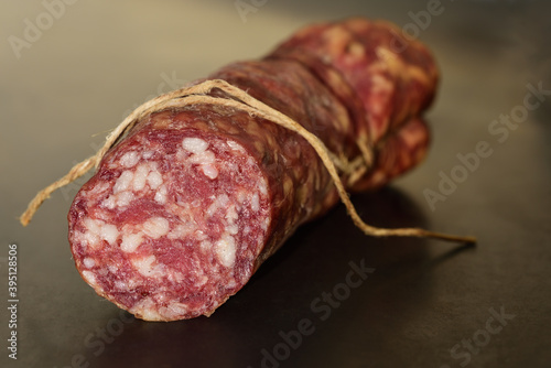 A salami in natural casing lies in front of a dark background, in landscape format