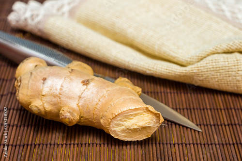 fresh ginger root on bamboo mat with knife and napkin, close-up