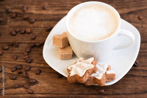 Fototapeta Naklejka Na Ścianę i Meble -  A cup, a mug of aromatic coffee with froth, sugar cubes and cookies on a saucer. Wooden background. Coffee shop advertisement, coffee break. Close-up