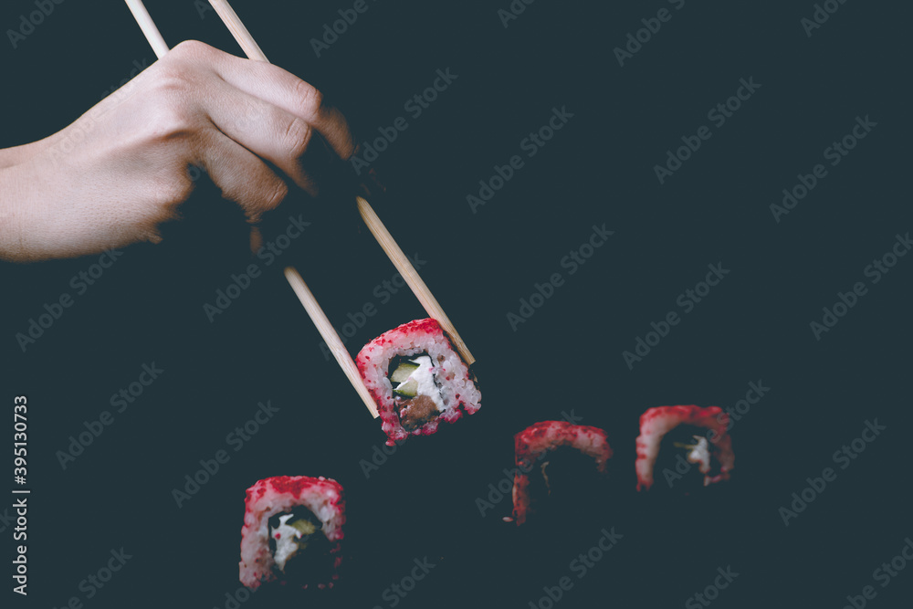 Female hand takes chopsticks california sushi rolls with Chinese chopsticks. Selective focus, black background Female hand takes chopsticks california sushi rolls with Chinese chopsticks. Selective focus, black background