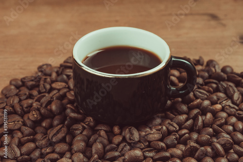 Vintage photograph of a cup of black espresso, accompanied by coffee beans on a wooden table © Marco
