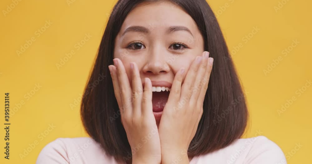 Close up of young amazed asian lady opening mouth and touching face in astonishment, yellow studio background Close up of young amazed asian lady opening mouth and touching face in astonishment, yellow studio background
