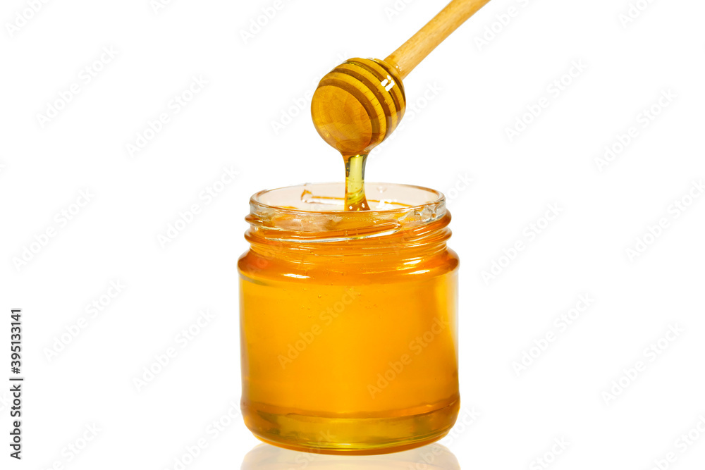 Honey dripping from honey dipper into glass jar isolated on white. Close-up. Healthy organic thick honey Honey dripping from honey dipper into glass jar isolated on white. Close-up. Healthy organic thick honey