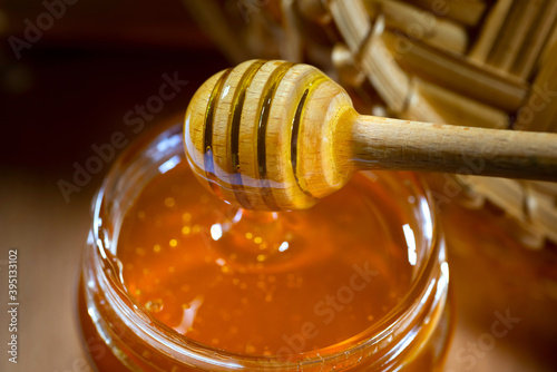 Honey drips from the honey bucket into a glass jar. Close-up. Healthy organic honey dipping from a wooden honey spoon, close-up