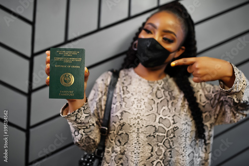 African woman wearing black face mask show Ghana passport in hand. Coronavirus in Africa country, border closure and quarantine, virus outbreak concept.