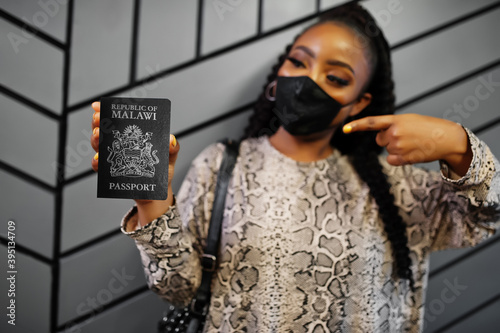 African woman wearing black face mask show Malawi passport in hand. Coronavirus in Africa country, border closure and quarantine, virus outbreak concept. photo