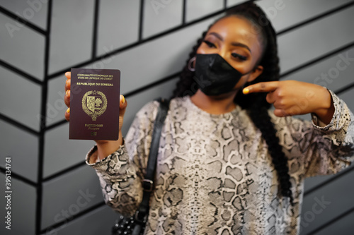 African woman wearing black face mask show Senegal passport in hand. Coronavirus in Africa country, border closure and quarantine, virus outbreak concept. photo