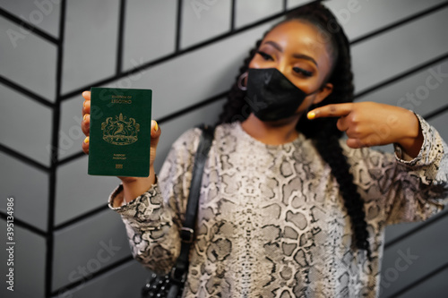 African woman wearing black face mask show Lesotho passport in hand. Coronavirus in Africa country, border closure and quarantine, virus outbreak concept. photo