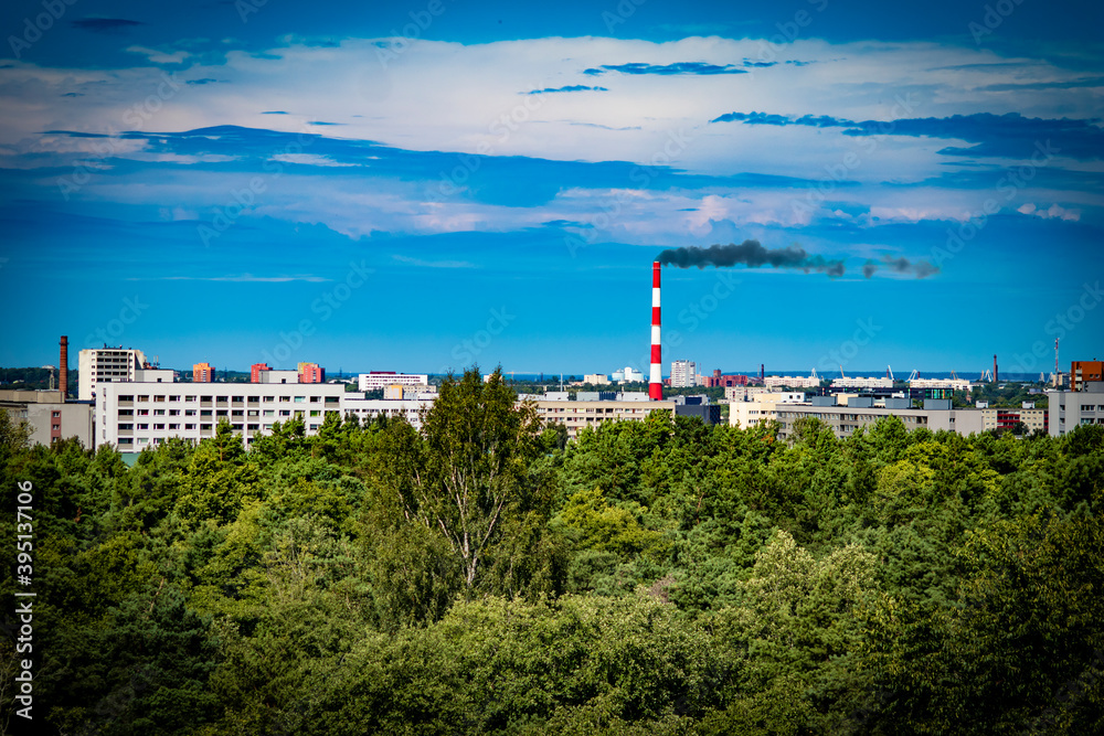 Retro cityscape with blockhouses, apartment buildings and  black smoke coming out of factory chimney with green trees in the foreground