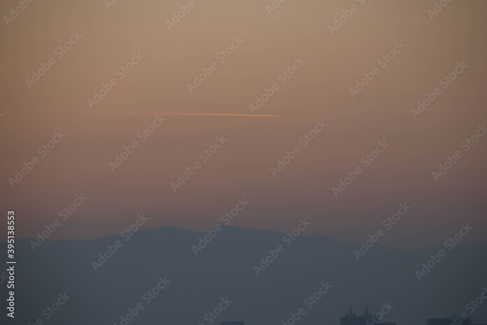 Close up of a sunset golden sky with a trace of the airplane and the hill.