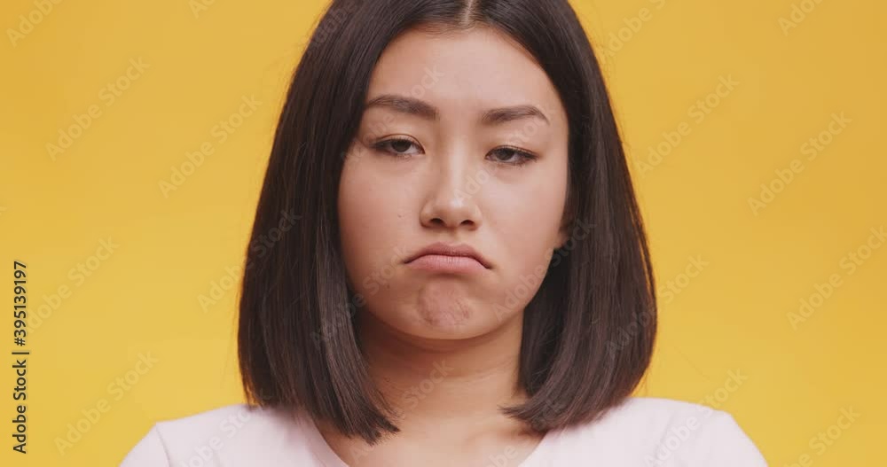 Studio portrait of unhappy depressed young asian woman pouting lips, looking sadly, orange background, close up