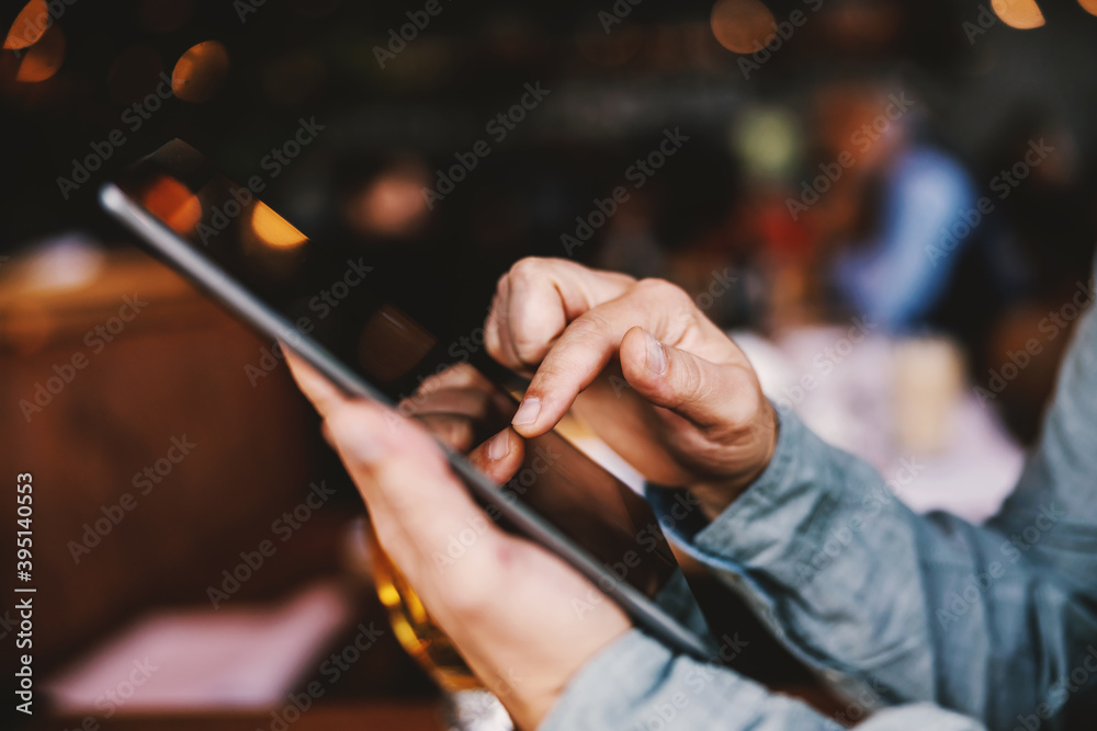 Closeup of man sitting in a bar and using tablet. Selective focus on finger.