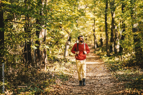Full length of young bearded cheerful explorer walking in the forest on a beautiful autumn day. Man is having backpack on backs. © dusanpetkovic1