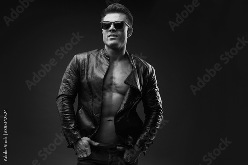 Sexy young man. Black and white portrait of guy in leather jacket with naked sexy torsoon dark backgound. High fashion model posing in studio. Free space for text.