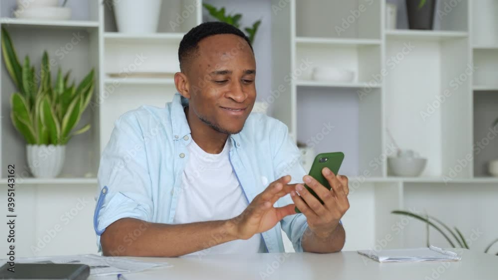 Young mixed race man sitting at table, reading sms on smartphone. Focused millennial businessman checking email in mobile application, communicating with partners. Young mixed race man sitting at table, reading sms on smartphone. Focused millennial businessman checking email in mobile application, communicating with partners.