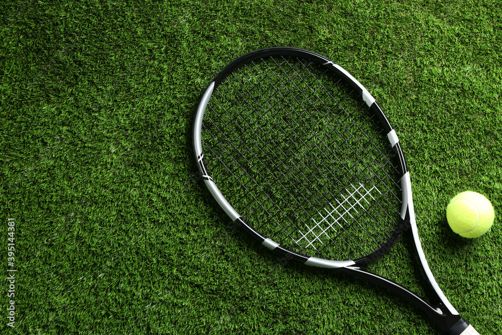 Tennis racket and ball on green grass, flat lay. Space for text