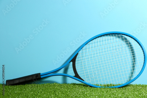 Tennis racket on on green grass against light blue background. Space for text