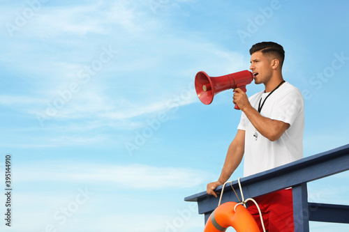 Male lifeguard with megaphone on watch tower against blue sky photo