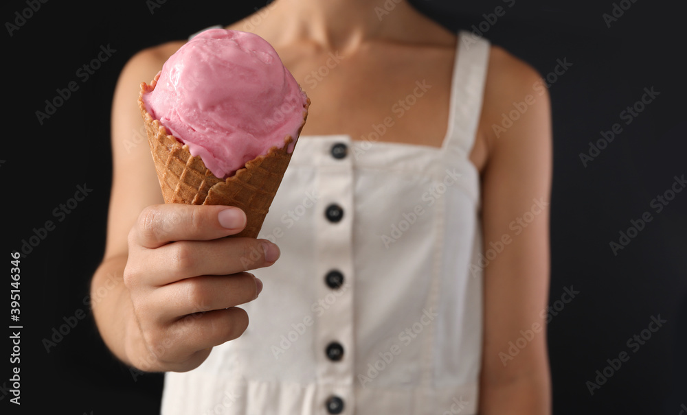 Woman holding pink ice cream in wafer cone on black background, closeup