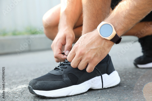 Man with fitness tracker tying shoelaces outdoors, closeup