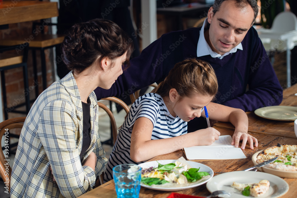 A girl doing her homework at the kitchen table with her parents being around. A girl doing her homework at the kitchen table with her parents being around.