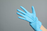 Doctor wearing medical gloves on grey background, closeup. Space for text