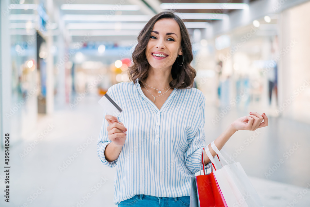 Portrait of happy smiling beautiful young woman walking in the mall with a credit card and shopping bags in hands