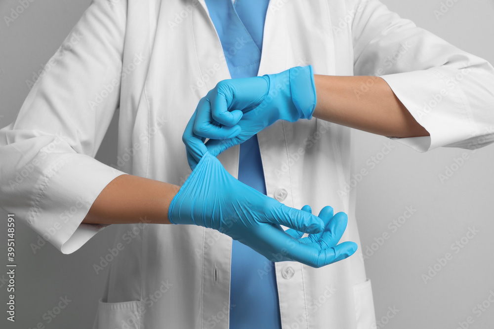 Doctor putting on medical gloves against light grey background, closeup Doctor putting on medical gloves against light grey background, closeup