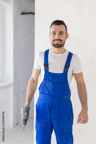 Repairer in blue overalls posing with a drill
