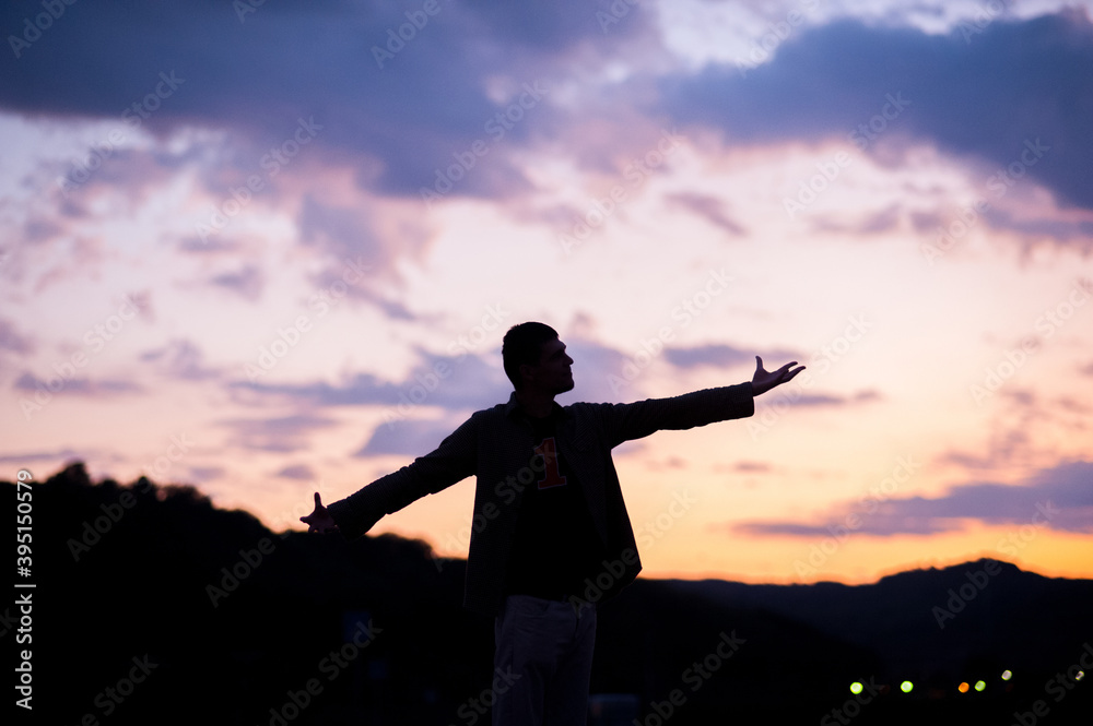 Man silhouette in front of a beautiful purple cloudy sky and orange sun rays Man silhouette in front of a beautiful purple cloudy sky and orange sun rays