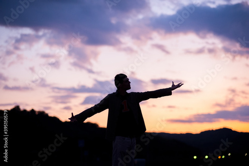 Man silhouette in front of a beautiful purple cloudy sky and orange sun rays 