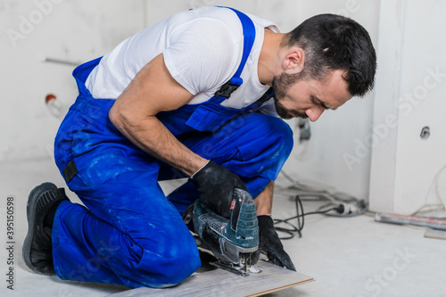 Carpenter in blue uniform cuts laminate flooring with a jigsaw. Medium shot
