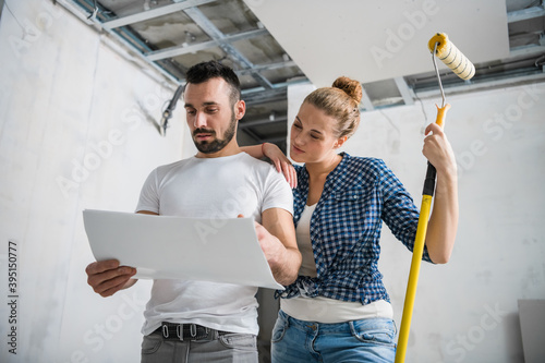 A woman holds a roller in her hand and hugs her husband. They look at the apartment layout photo