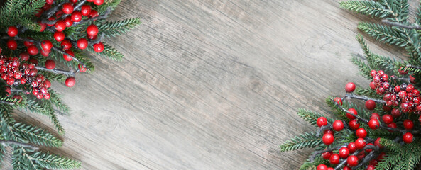 Christmas Evergreen Pine Branches and Red Berries in Corners Over Wood Background. Holiday Garland Border Backdrop with Copy Space. Greenery and Winter Berries Xmas Frame Over Light Wooden Texture.