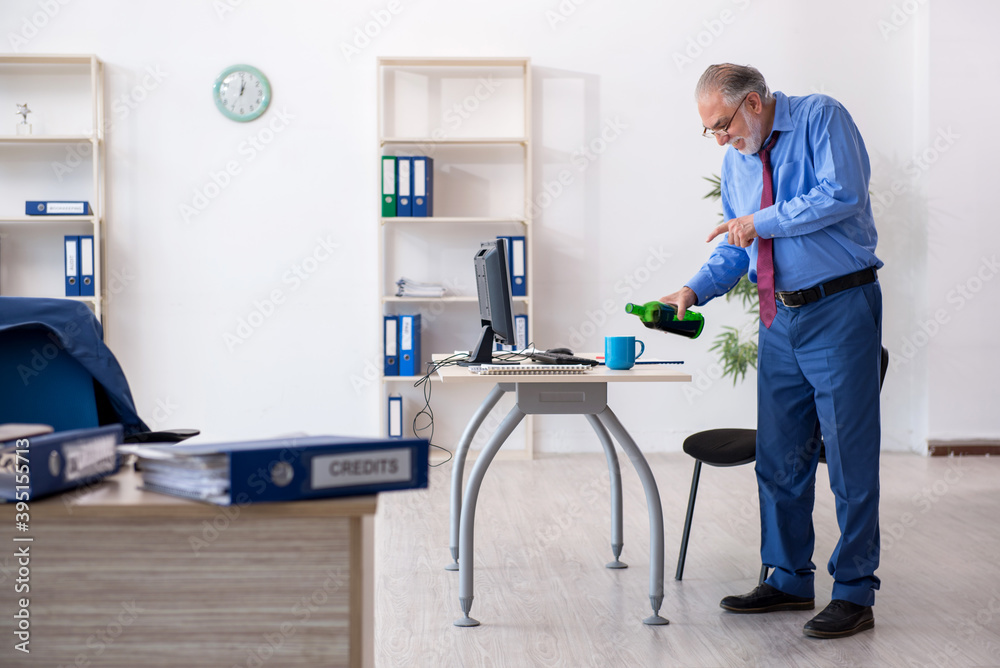 Old male employee drinking alcohol in the office