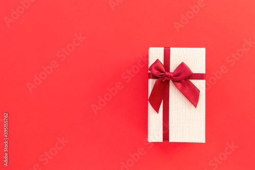 Gift in a box with a bow on red background. Top view, flat lay, copy space.