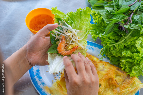 Fototapeta Naklejka Na Ścianę i Meble -  Woman's hands wrapping food with lettuce while eating Banh Xeo 