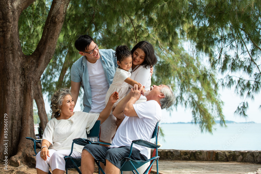 Group of Healthy multi generation Asian family enjoy picnic travel together on the beach. Parents with cute child girl and healthy senior grandparents relax and having fun on summer holiday vacation