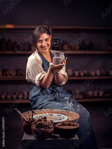 Beautiful young and cheerful woman shows how to work with clay and pottery wheel. Handiwork.