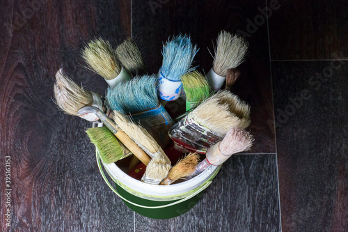 A set of used brushes in a bucket for repair, multicolored after painting, stand on the floor