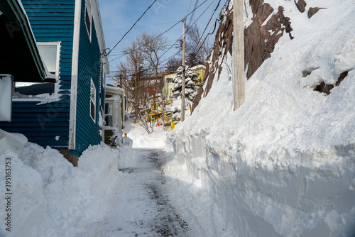 St. John's, Newfoundland Canada- November 2020: A narrow street covered in fresh white snow and deep snow from a snowstorm with bright painted colourful wooden clapboard style houses on Signal Hill.  photo