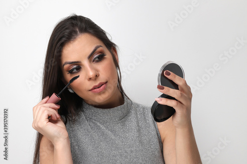 Beautiful girl putting on makeup on white background