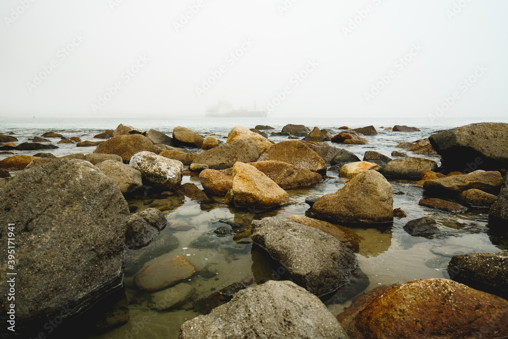 Quiet water, seashore rocks, and silhouette of vessel on a horizon at an overcast day Quiet water, seashore rocks, and silhouette of vessel on a horizon at an overcast day