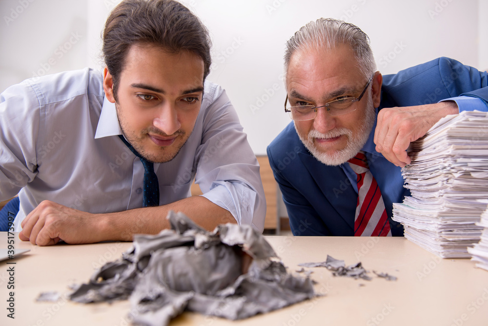 Young male employee and old boss burning papers at workplace Young male employee and old boss burning papers at workplace