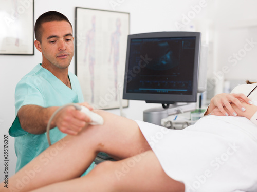 Young man sonographer using ultrasonography machine checking female patient in hospital diagnostic room