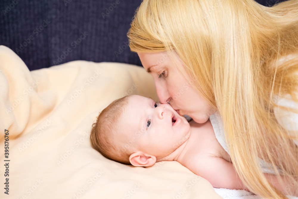 Natural Portrait of Young Caucasian Mother Kissing Her Newborn Baby Boy Lying on Bed. Natural Portrait of Young Caucasian Mother Kissing Her Newborn Baby Boy Lying on Bed.