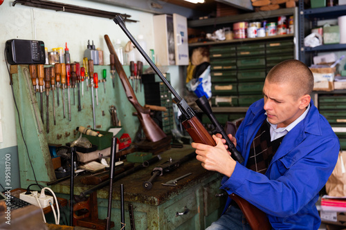 Skilled gunsmith installing optical sight on smallbore single-barreled rifle in weapons workshop
